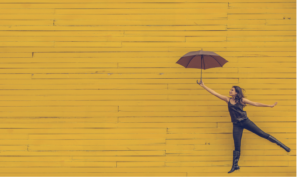 Employee thriving is the new employee engagement - happy female jumping with umbrella against painted yellow backdrop