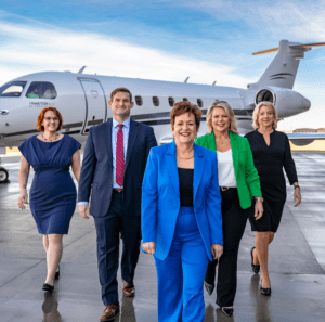 Outside scene at airport with five business aviation recruiters wearing professional business attire, walking toward camera away from a parked Praetor 600 business jet - From left: Michaela Heacox, Ben Janaitis, A&P, Sheryl A. Barden CAM, Jennifer E. Pickerel and Christine Wetherell from Aviation Personnel International, a 50-year-old recruitment firm.